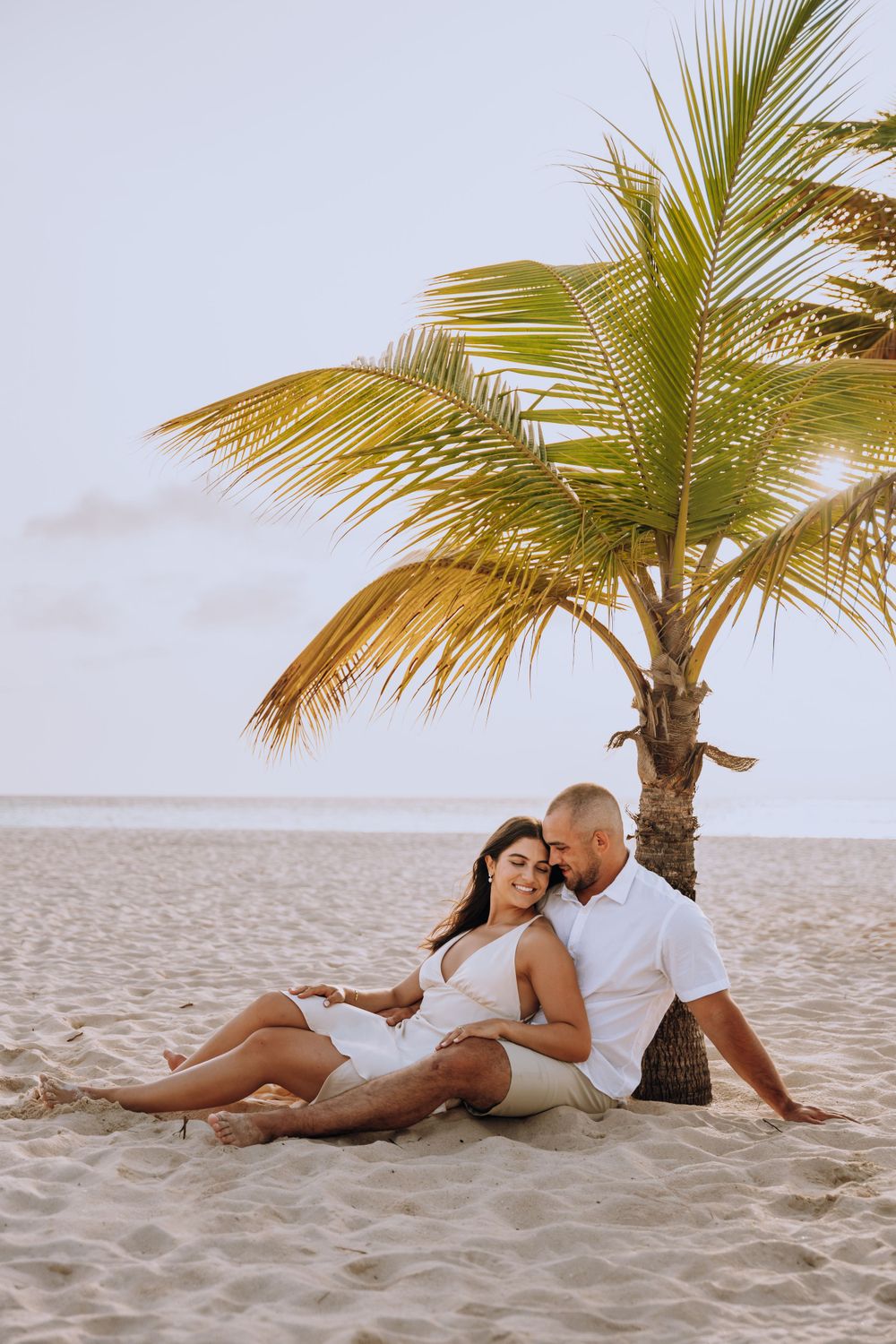 Couple relaxing together on a tropical beach under a palm tree at sunset.