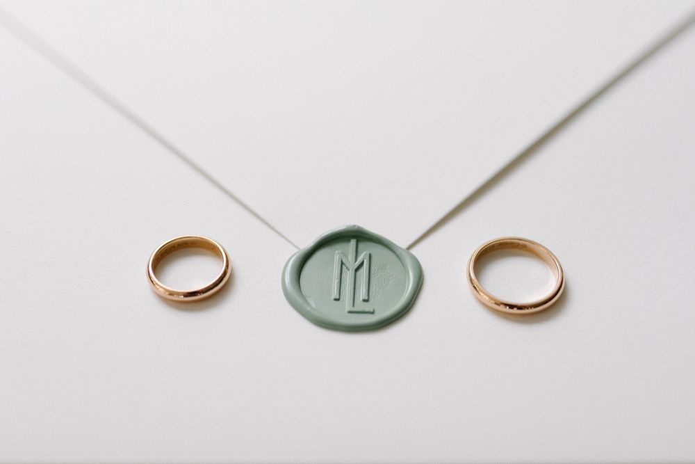 Two gold wedding bands and a mint green wax seal on a white envelope.