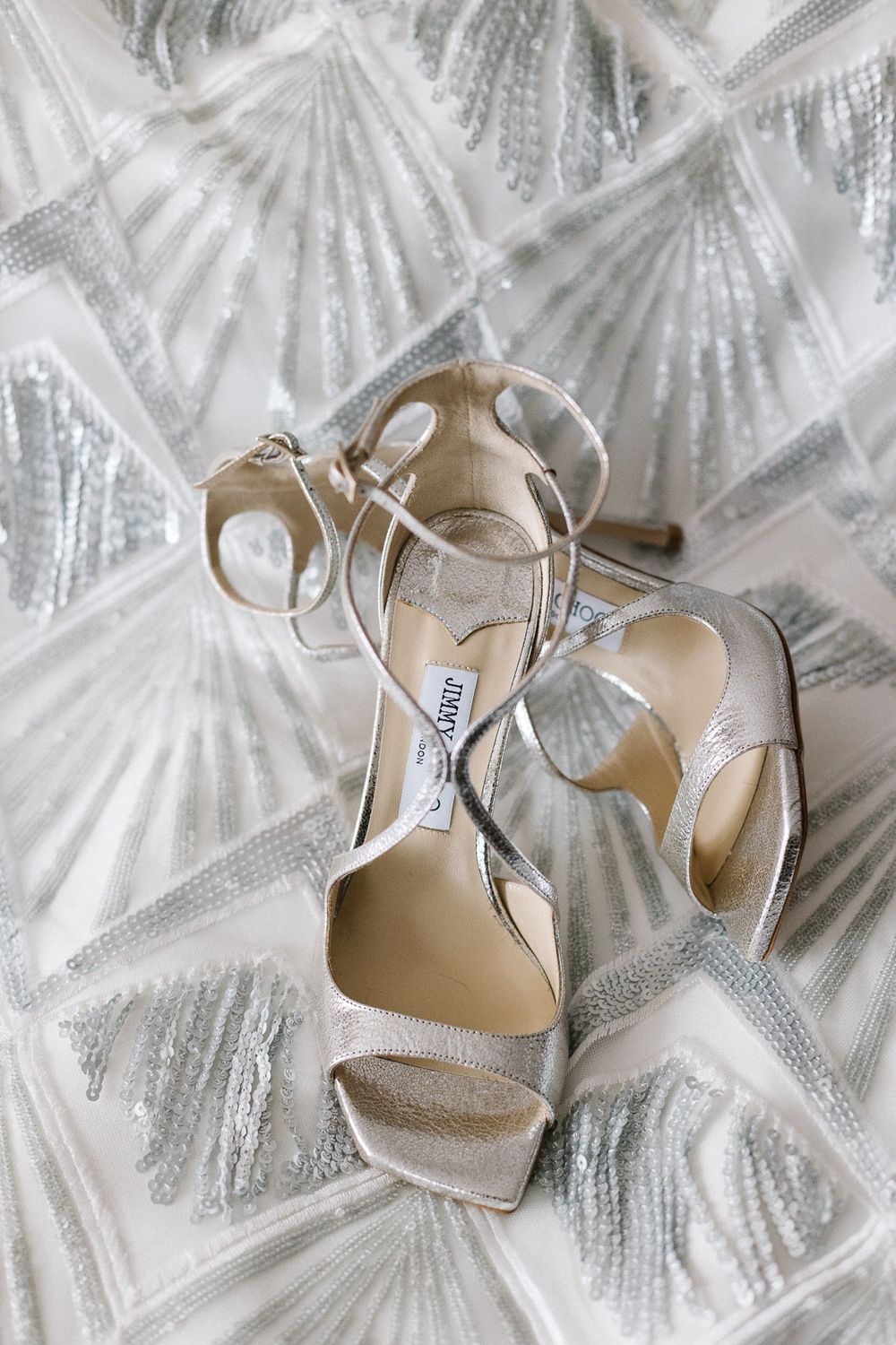 Jimmy Choo silver strappy wedding sandals displayed on beaded fabric.