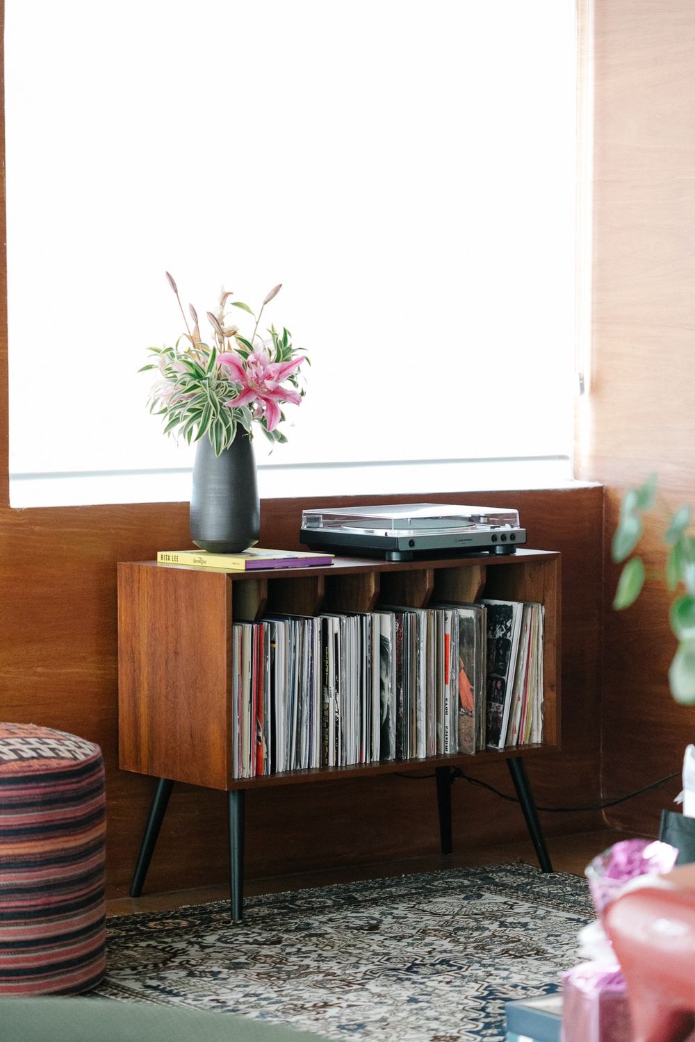 Mid-century modern record cabinet with turntable and flower vase displayed in a cozy living room corner.