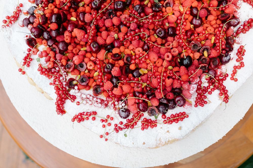 Fresh red berries and fruits decorating the top of a white frosted cake.