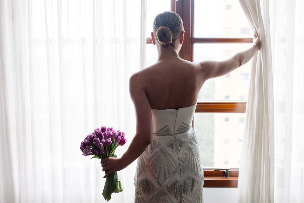 Silhouette by window holding purple flowers in white formal dress.