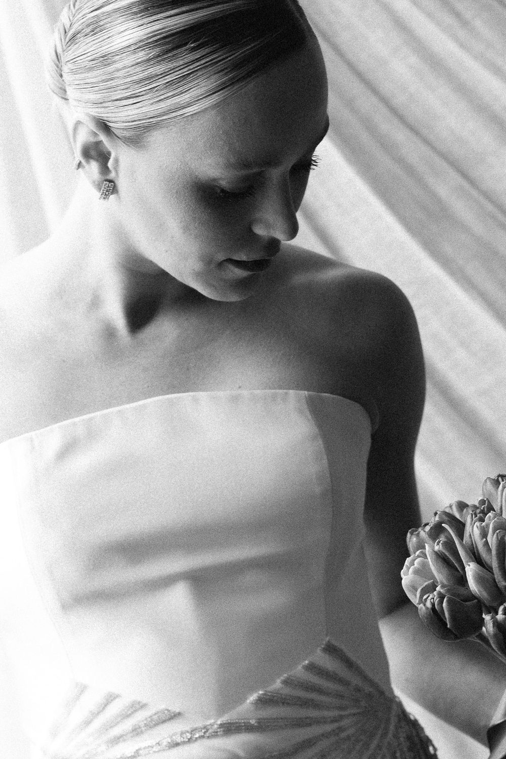 Intimate black and white portrait of someone wearing a strapless wedding gown with a delicate floral bouquet.