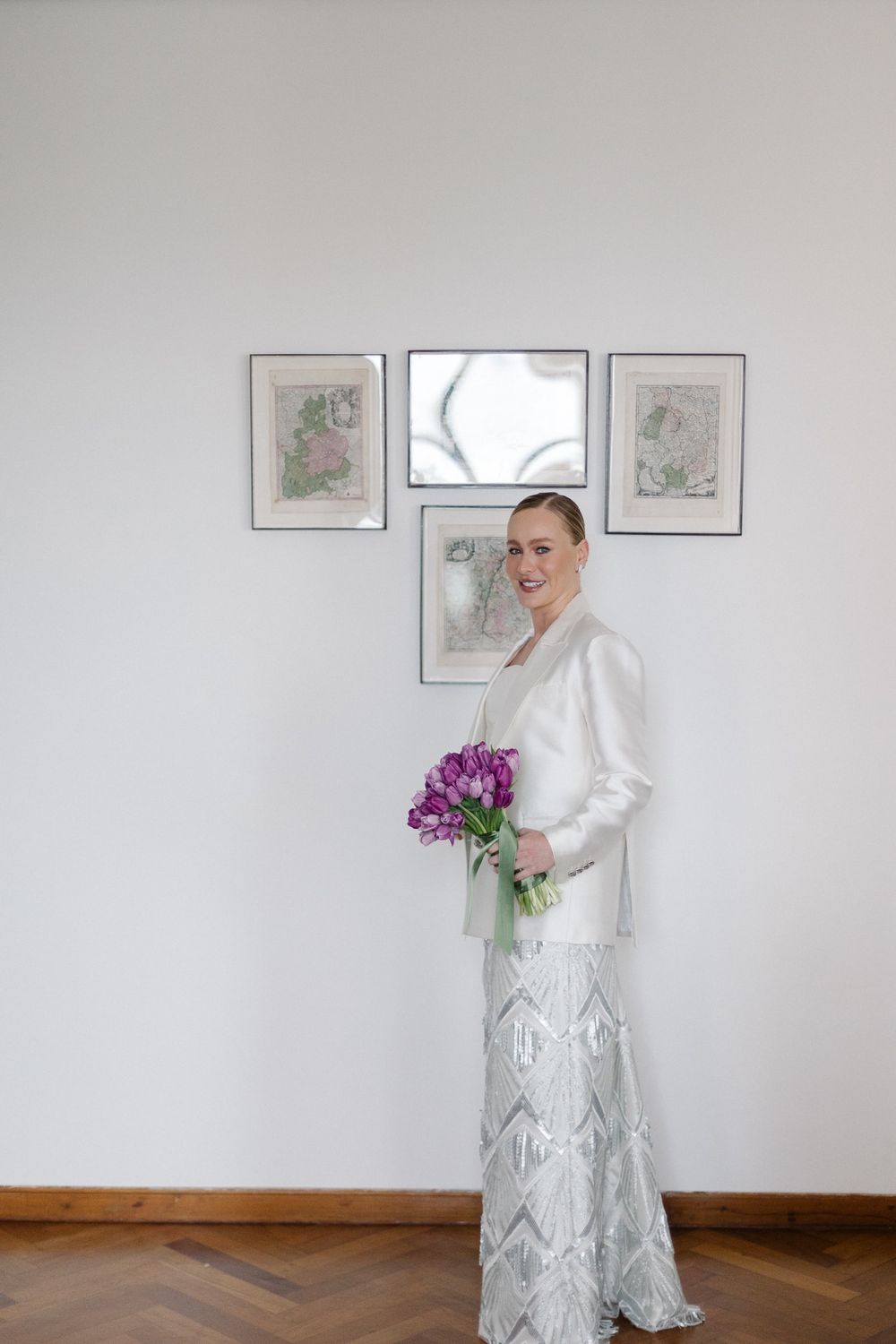 Modern bridal look featuring a white blazer and lace dress with vibrant purple tulips against a minimalist wall.
