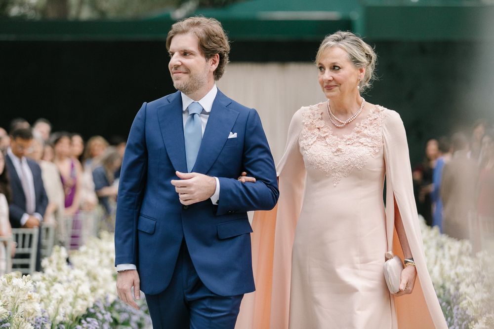 Wedding couple walking together, with soft peach and navy attire at an outdoor celebration.