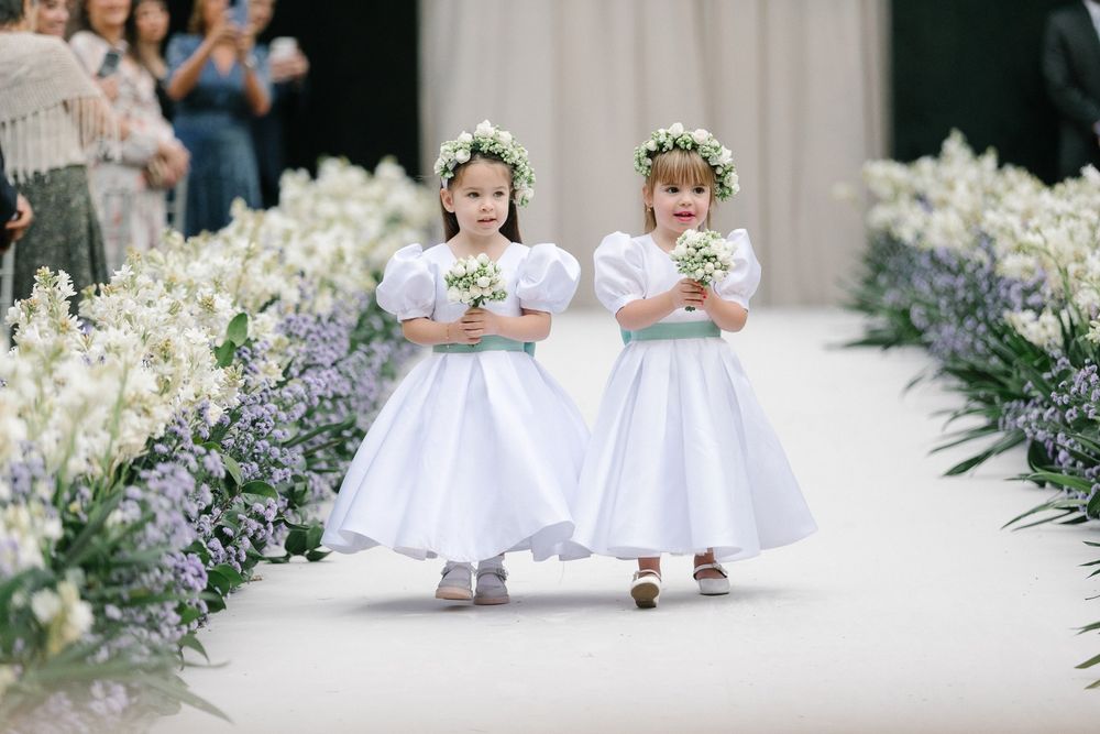 Two flower girls in white dresses walk down a floral-lined aisle.