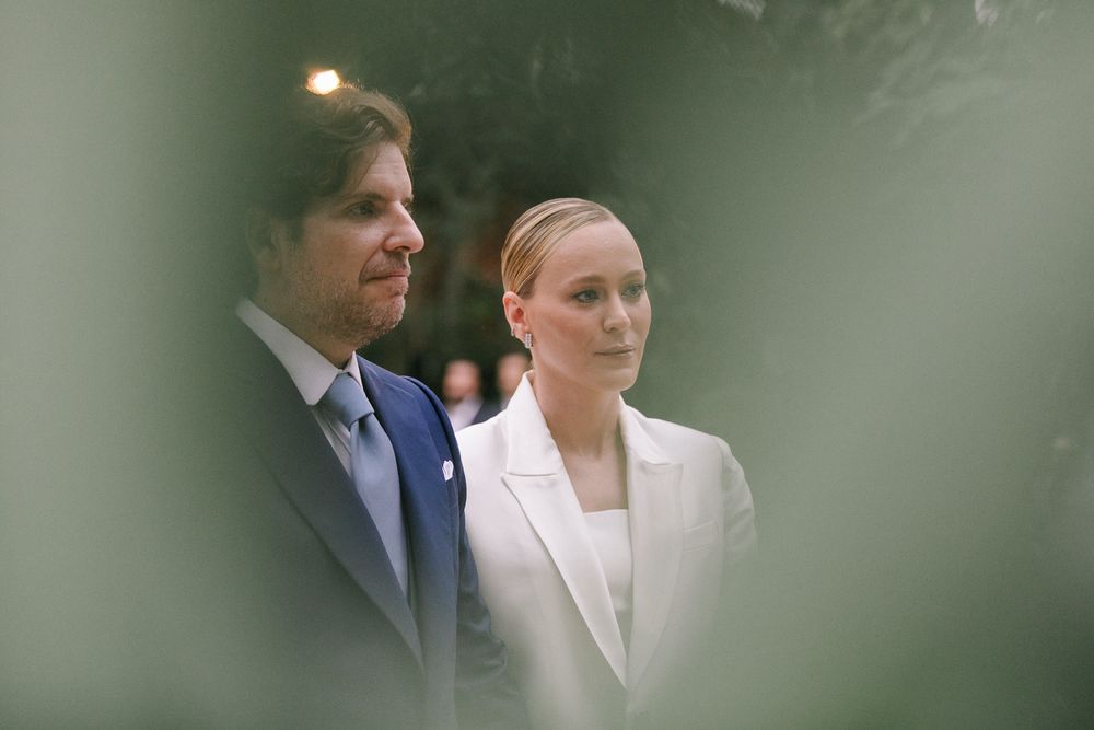 A couple shares an intimate moment outdoors through soft focus foliage at an elegant event.