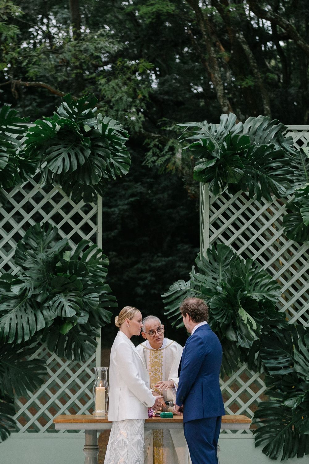 A wedding ceremony setup with tropical leaves and white lattice backdrop in a garden setting.