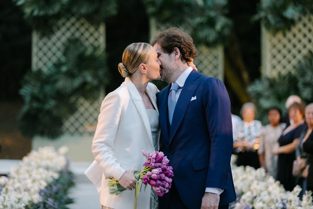 A romantic moment between newlyweds holding a purple bouquet in a garden setting.