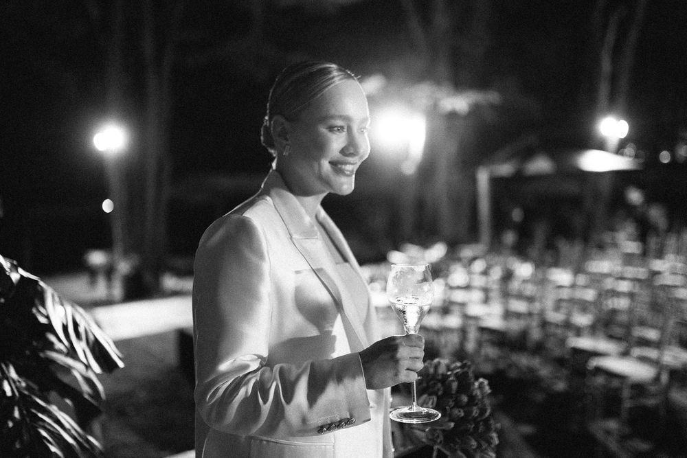 A black and white portrait of someone in formal attire holding a drink at night.