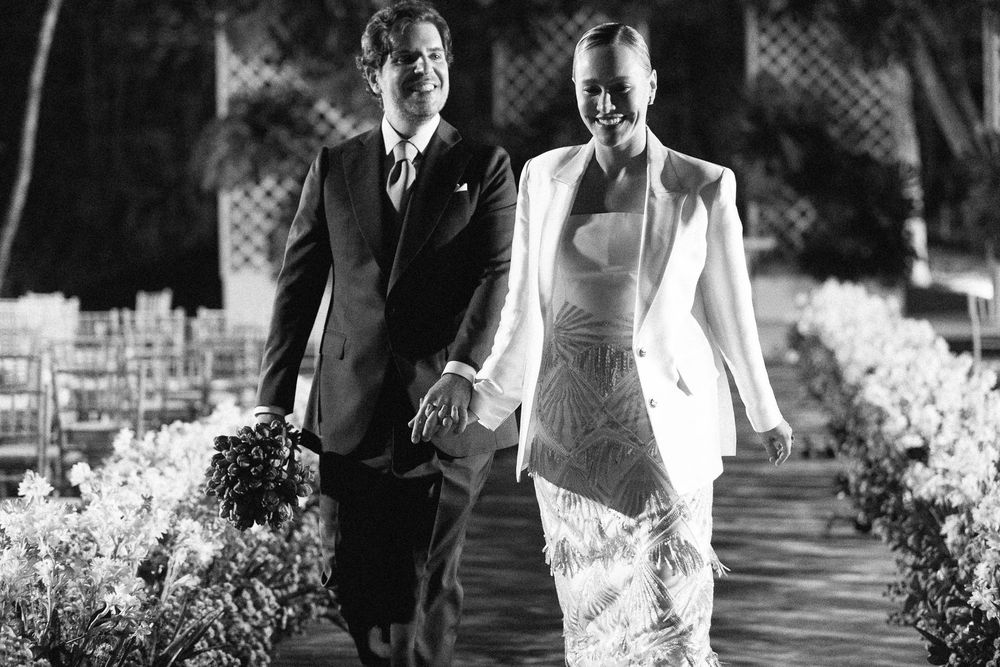 A black and white photograph showing a couple walking together on a garden path after their wedding ceremony.