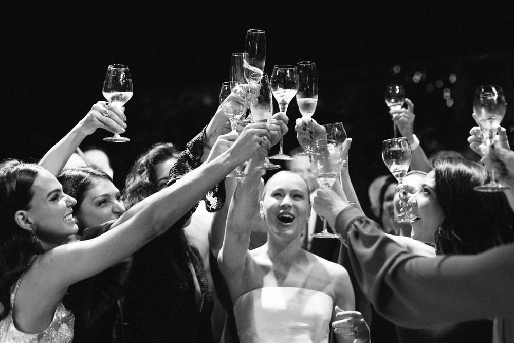 Black and white photo of wedding guests raising champagne glasses in a celebratory toast.