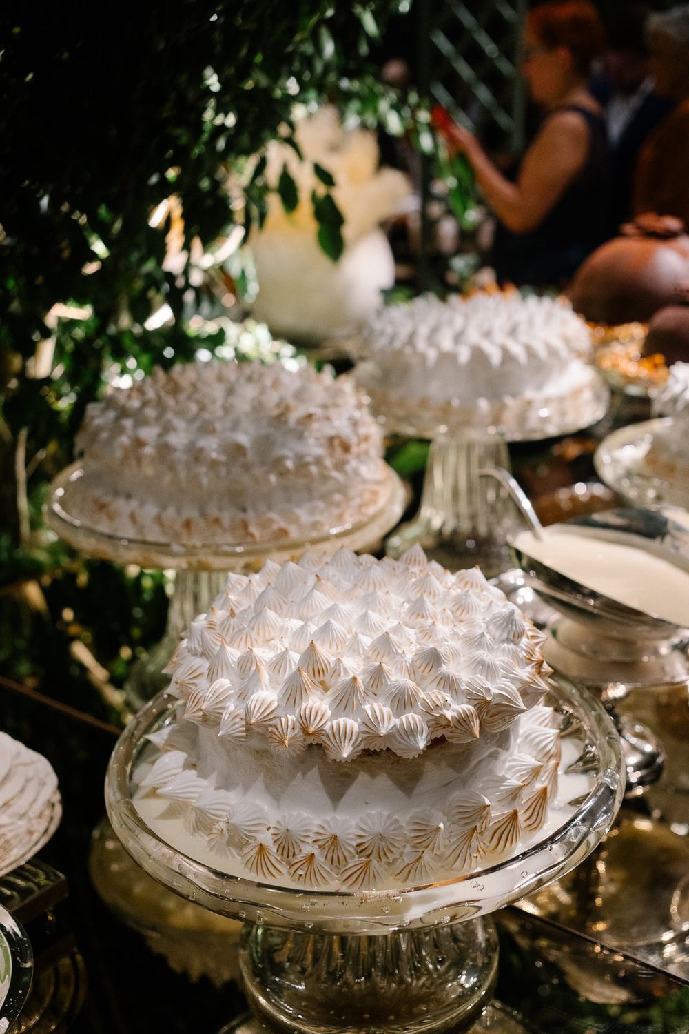 Ornate white wedding cakes with intricate piped designs displayed on crystal pedestals.