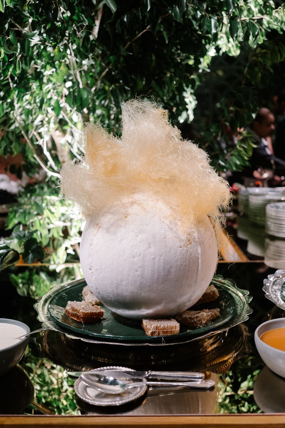 Whimsical dessert featuring cotton candy cloud atop a plated dish surrounded by greenery.