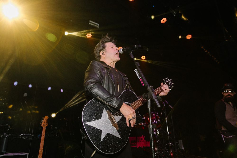 Musician performing on stage with acoustic guitar under dramatic lighting.