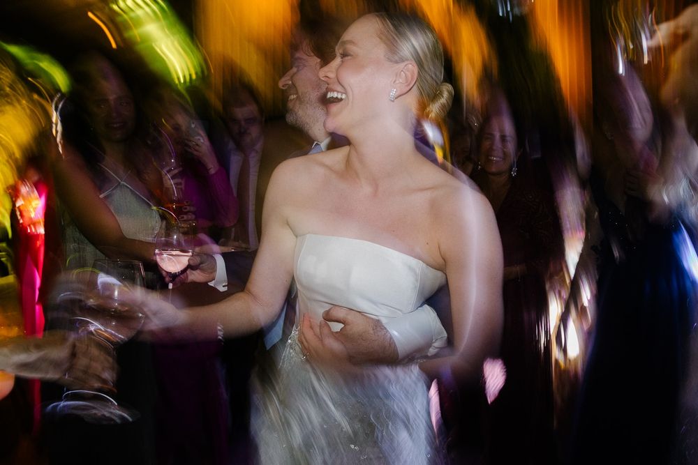 A person in a white dress dances joyfully at a lively reception.
