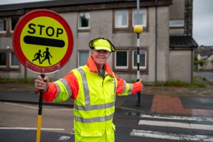A crossing guard in high-visibility yellow safety gear holds up a stop sign at a pedestrian crossing.