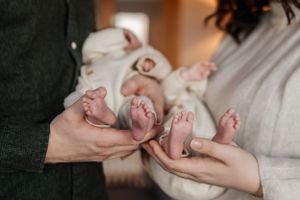 Close-up of tiny baby feet being held by two sets of adult hands in gentle, supporting gesture.