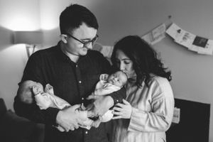 A tender black and white image of parents caring for their newborn baby in a softly lit room.