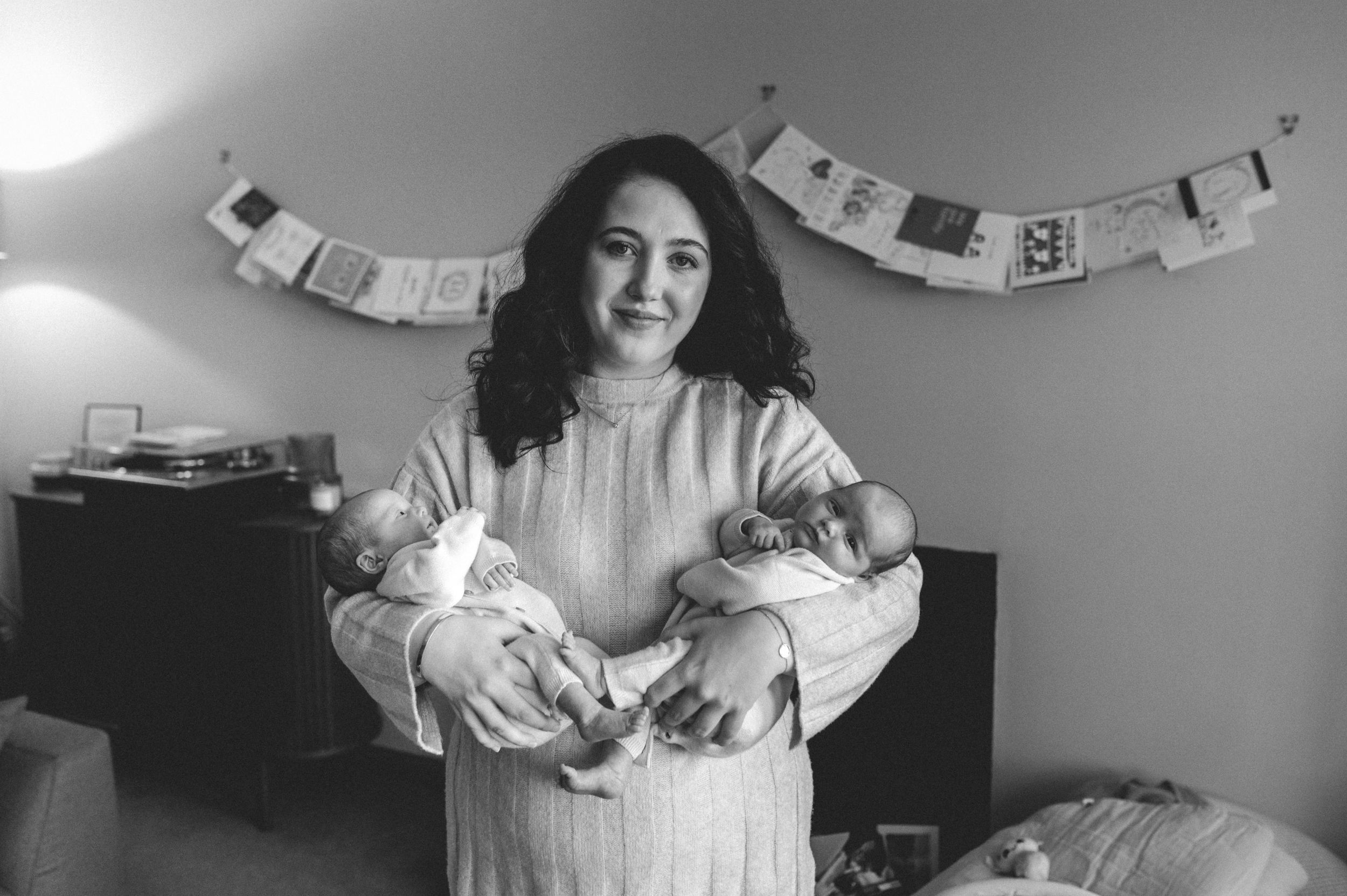 A woman in a white dress cradles two small kittens in her arms while standing in front of a decorative banner.