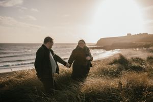 Two people hold hands while walking along a scenic coastal path during golden hour sunset.