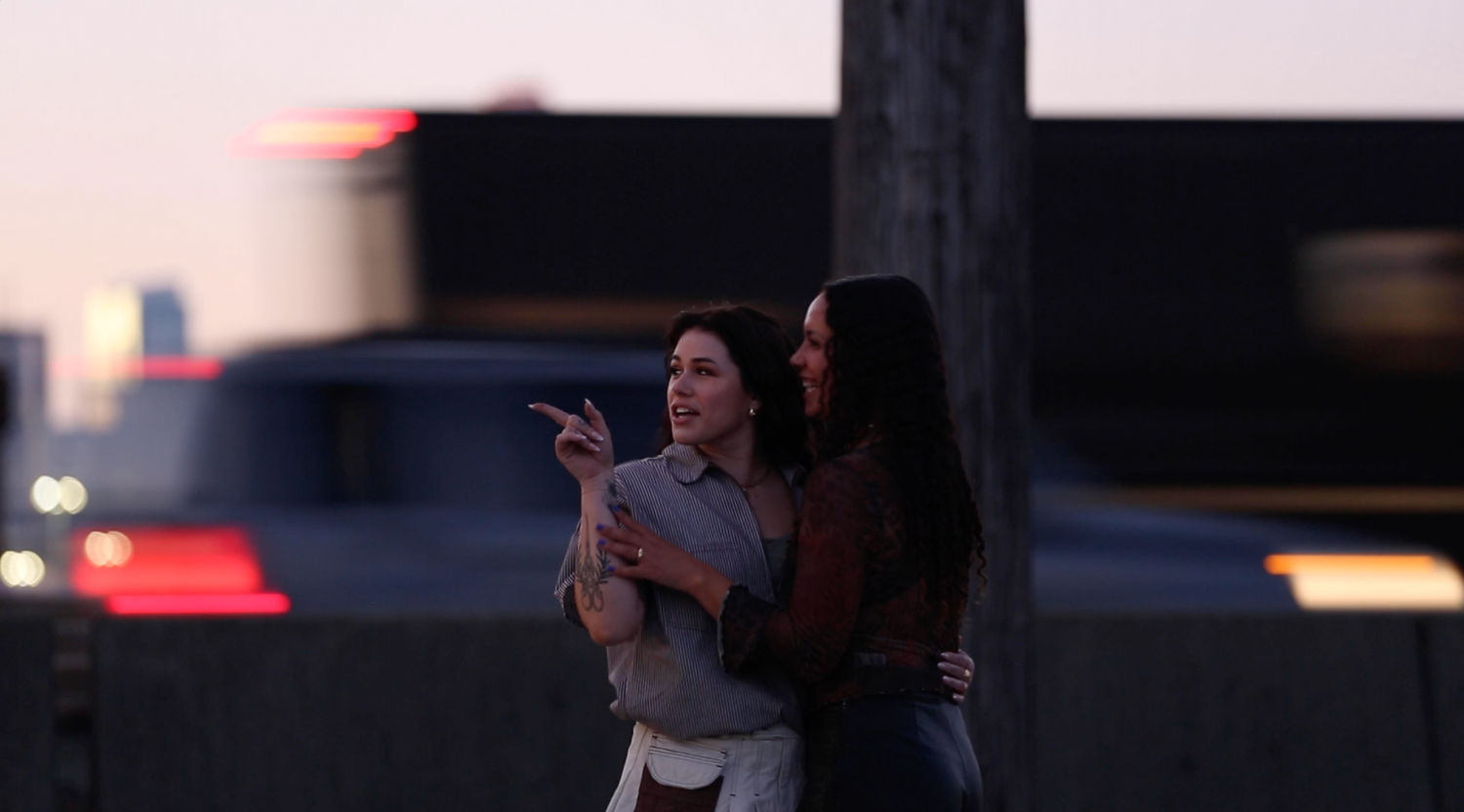 Two people stand together outdoors at dusk while pointing towards something in the distance.