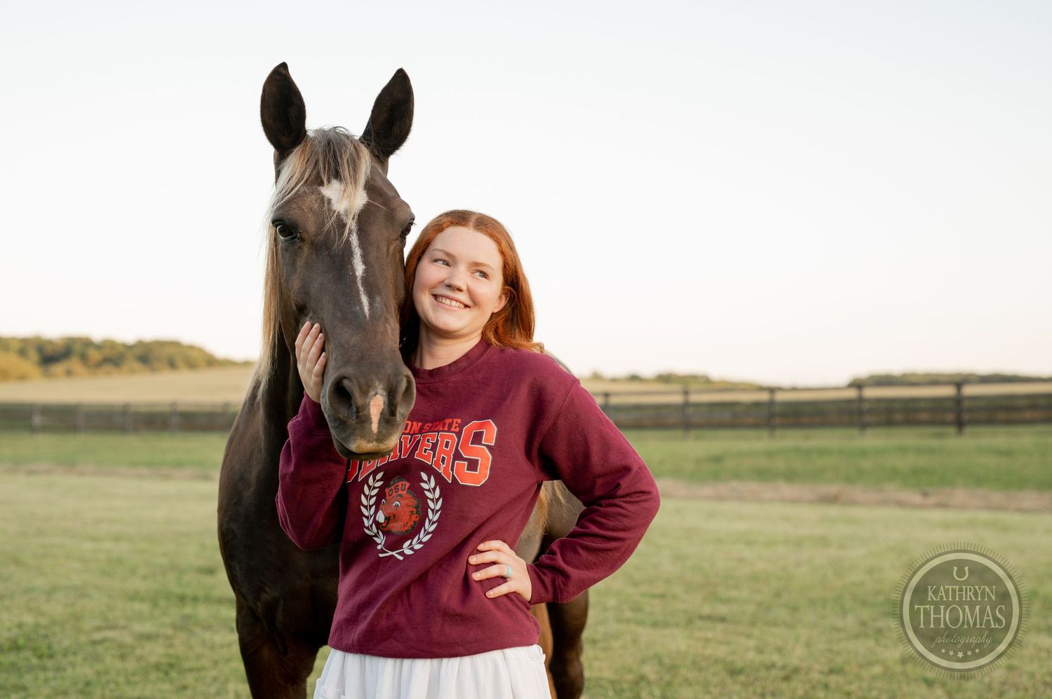 A dark horse stands with someone wearing a burgundy sweatshirt in a grassy field.