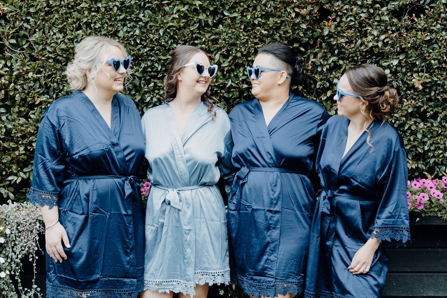 Bride and bridesmaids wearing matching navy blue silk robes with their sunnies, captured by Apertured Media Auckland Wedding Photographer.