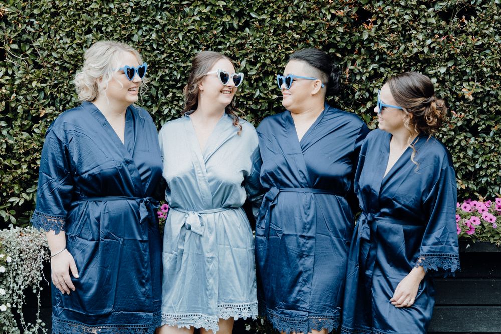 Bride and bridesmaids wearing matching navy blue silk robes with their sunnies, captured by Apertured Media Auckland Wedding Photographer.