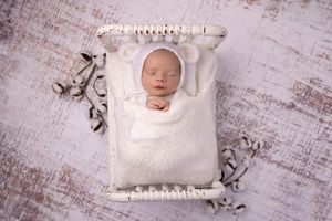 A series of delicate newborn photography images showing a sleeping baby wrapped in soft white fabric against a rustic backdrop.