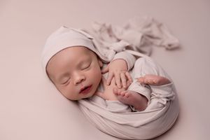 Peaceful newborn baby sleeping peacefully while wrapped in soft white swaddling blanket during professional photo session.