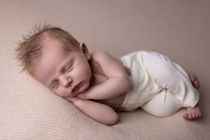A sleeping baby lies peacefully on white fabric in a gentle curled position.