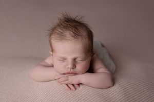 A sleeping newborn baby rests peacefully on soft textured fabric in warm neutral tones.