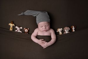 Newborn baby resting on dark backdrop surrounded by small plush animal toys.