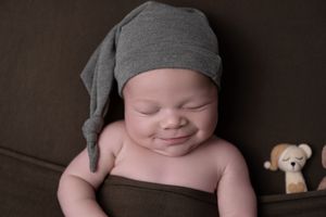 Sleeping baby wearing gray hat photographed with stuffed animal toys in dark studio setting.