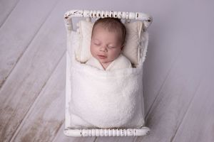 A sleeping newborn baby swaddled in white fabric lies on a cozy blanket during a professional photo session.