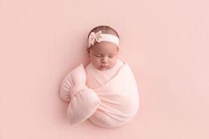 A collage of newborn baby photos in soft pink tones showing peaceful sleeping poses wrapped in delicate fabric.