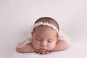 Sleeping newborn baby wearing white headband rests peacefully on soft blanket in professional studio setting.