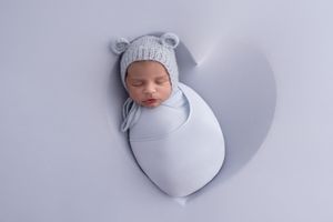 A sleeping newborn baby wrapped in soft gray swaddle blanket with matching hat on white background.