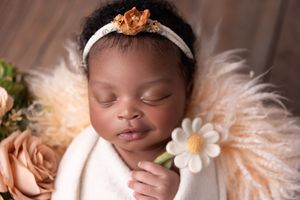 Sleeping newborn baby wearing peach headband with floral decorations in dreamy portrait session.