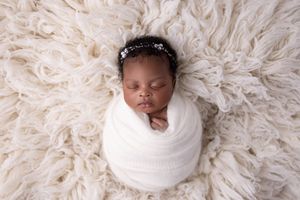 A sleeping newborn baby swaddled in white fabric lies on a soft cream-colored textured blanket.