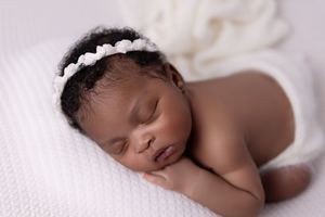 Sleeping newborn baby lying peacefully on white blanket in natural light during professional photoshoot.