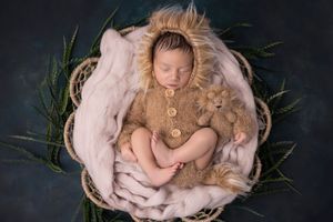 Newborn baby sleeps peacefully in a pink floral nest with delicate lace and natural greenery accents.