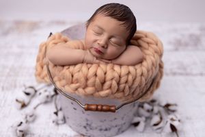 Newborn baby sleeping peacefully in soft knitted blankets and baskets during professional photo session.