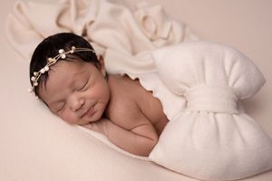 Peaceful sleeping newborn baby wrapped in soft white blankets on neutral beige background.