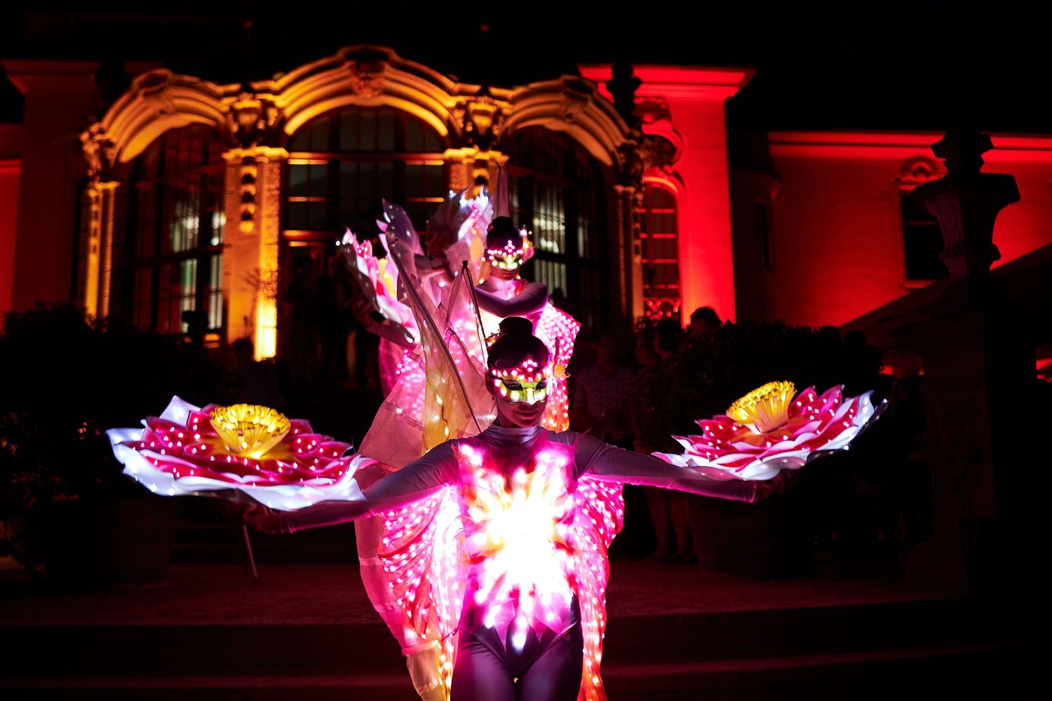 Colorful pink and red illuminated lantern displays shine brightly against dark night sky at a festival celebration.