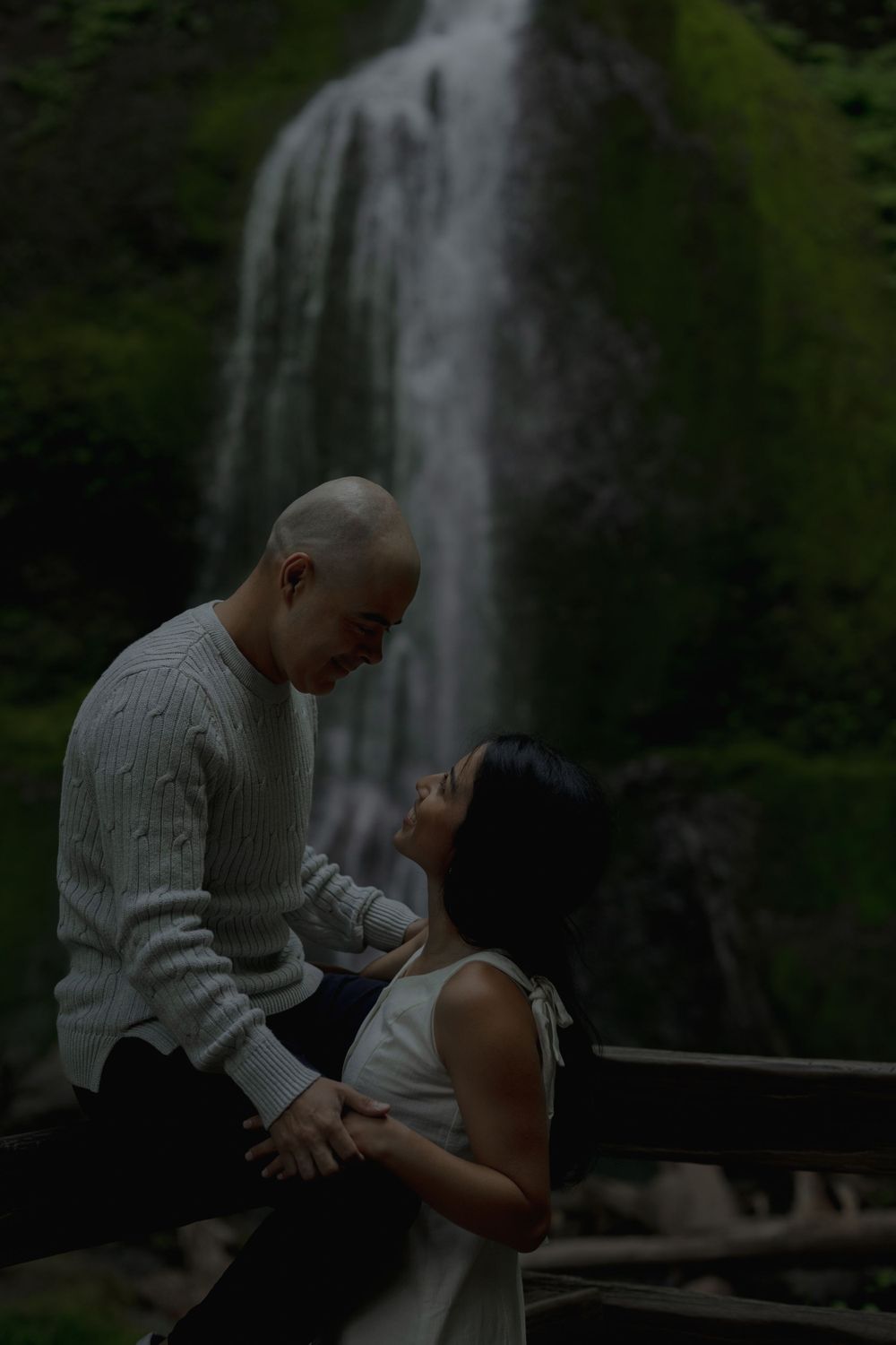 A couple shares an intimate moment on a viewing platform with a waterfall backdrop Marymere falls in Olympic National Park..
