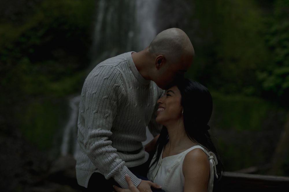 A tender embrace shared between two people with a misty waterfall in the background Marymere falls in Olympic National Park..