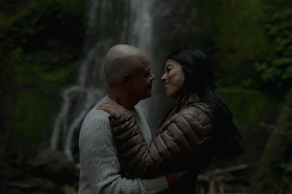 A couple shares an intimate moment in front of a misty forest waterfall at Marymere waterfall in Olympic National Park.