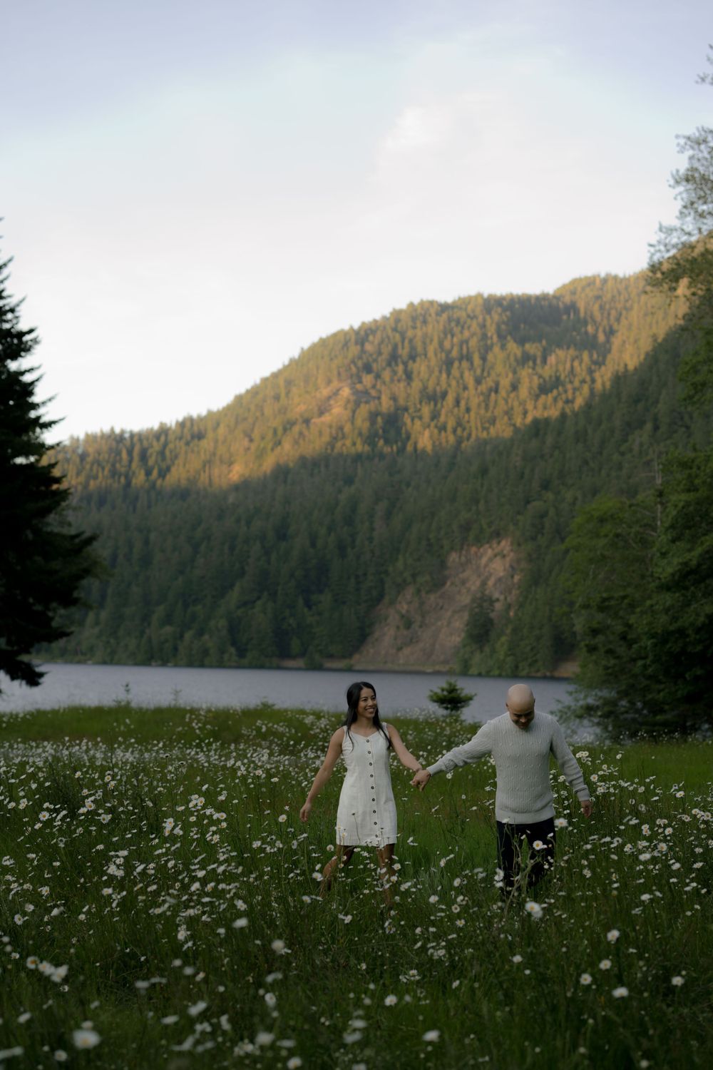 A couple walks through a wildflower meadow with mountain views and a lake in the background at lake crescent in Olympic national park.